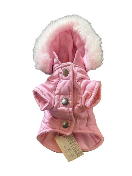 A pink quilted dog jacket with a fluffy white faux-fur trimmed hood, laid flat on a gray carpet. The jacket features three silver snap buttons on the front and a paper tag is attached near the bottom.