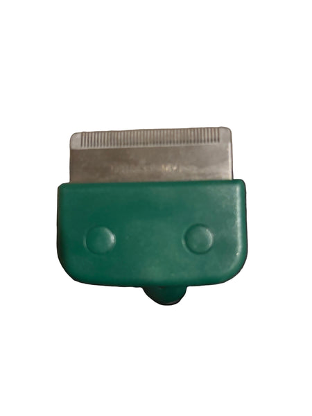 A close-up of a grooming tool with a green plastic handle and a silver metal blade, resting on dark gray fabric.